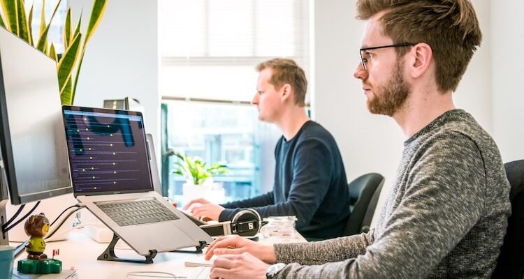 man sitting on chair wearing gray crew-neck long-sleeved shirt using Apple Magic Keyboard