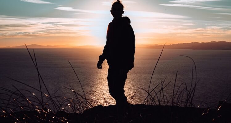 silhouette of man standing on hill during sunset