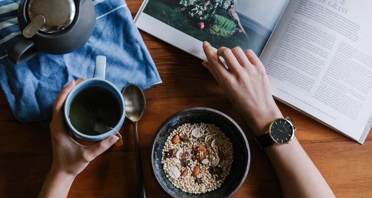 person holding blue ceramic mug and white magazine
