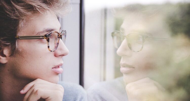 a man wearing glasses looking out a window